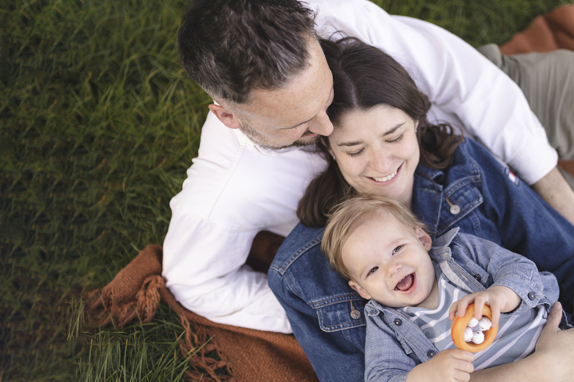 Family of three cuddling and laughing together on the grass in redhill common, surrey.